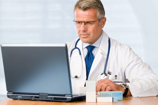 Male Gray Middle Aged Doctor Laptop 3 Cropped TOS Surgeon Reviews Different Surgical Approaches