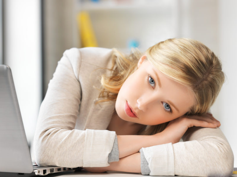 Blonde woman in pain with head on folded arms in front of laptop